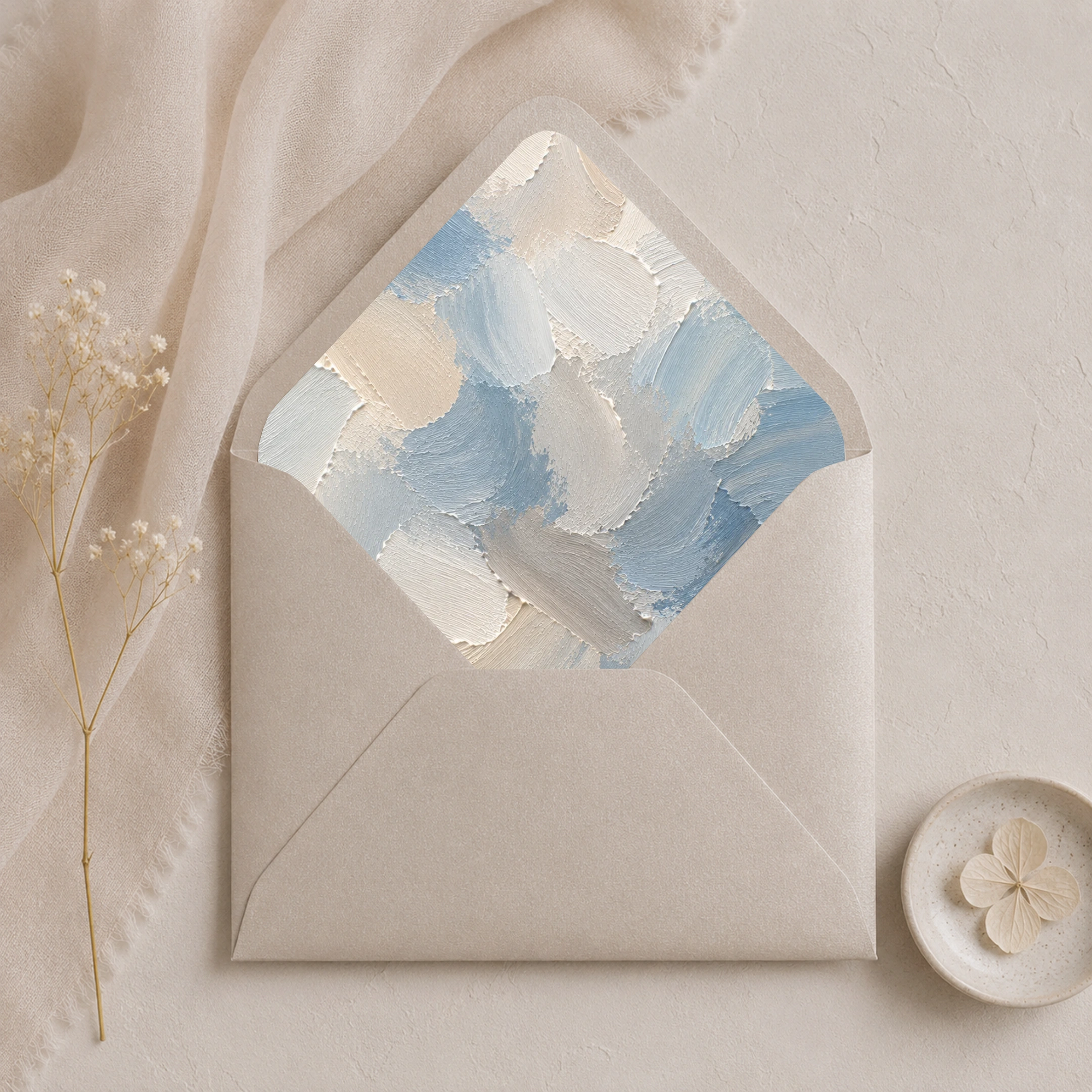 Dusty Canvas Envelope Liner Template displayed inside a metallic sand envelope, featuring painterly dusty blue, ivory, cream, and soft grey abstract brushstrokes for elegant wedding invitations.